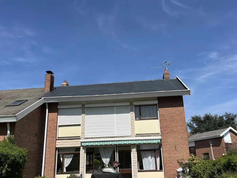 Maison en briques à toiture en ardoises propre, rives blanches et souches de cheminée